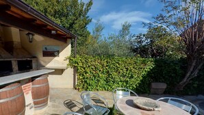 Une terrasse extérieure avec une table en pierre, des chaises en métal et un four en briques.