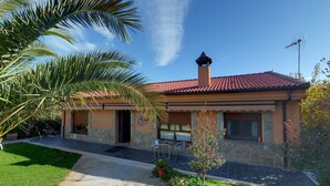 Une maison à deux étages, avec un toit recouvert de tuiles rouges, des murs en pierre et un petit porche agrémenté de chaises.
