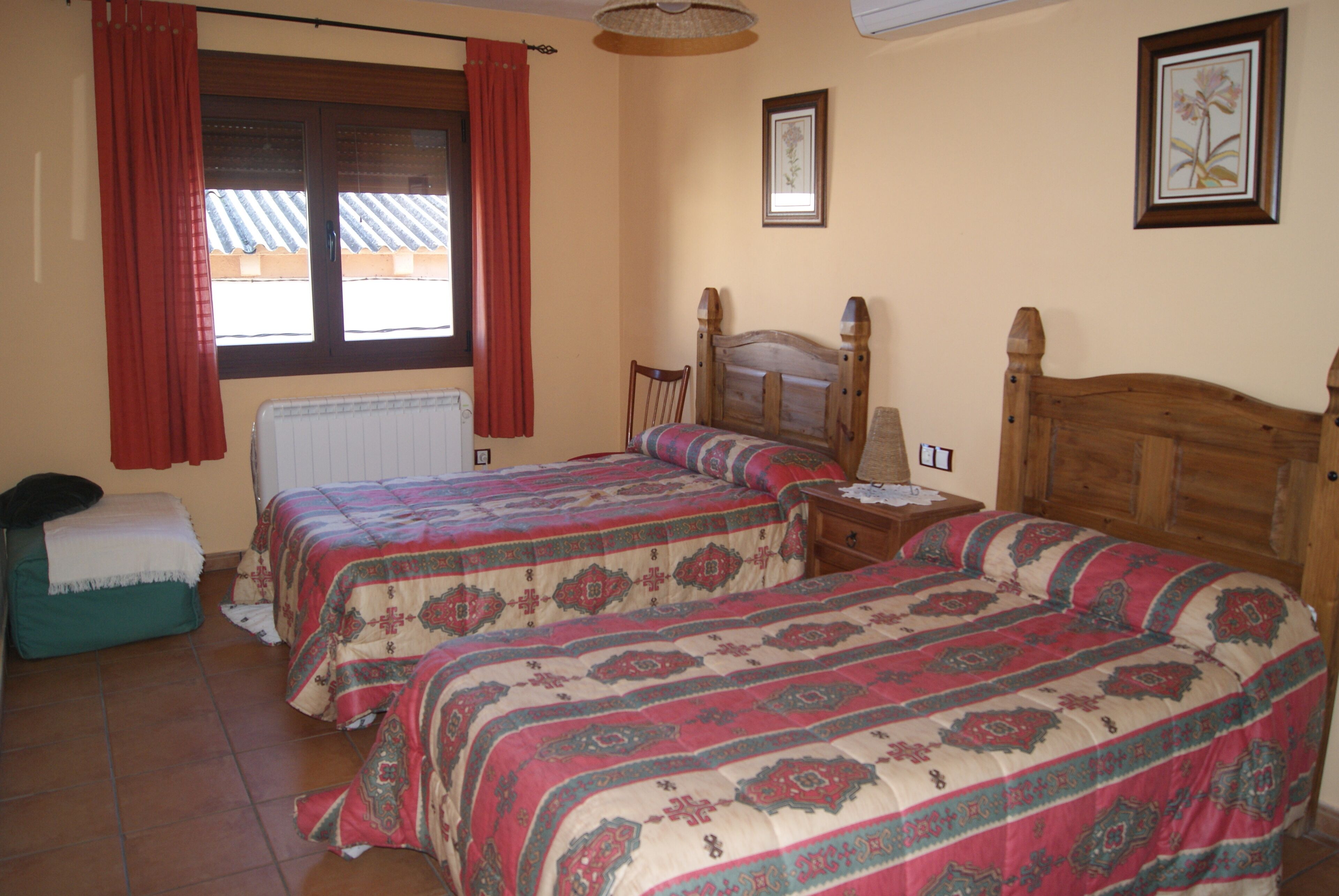 Un dormitorio con dos camas, una ventana con cortinas, un radiador, un cabecero de madera y un cuadro enmarcado en la pared.