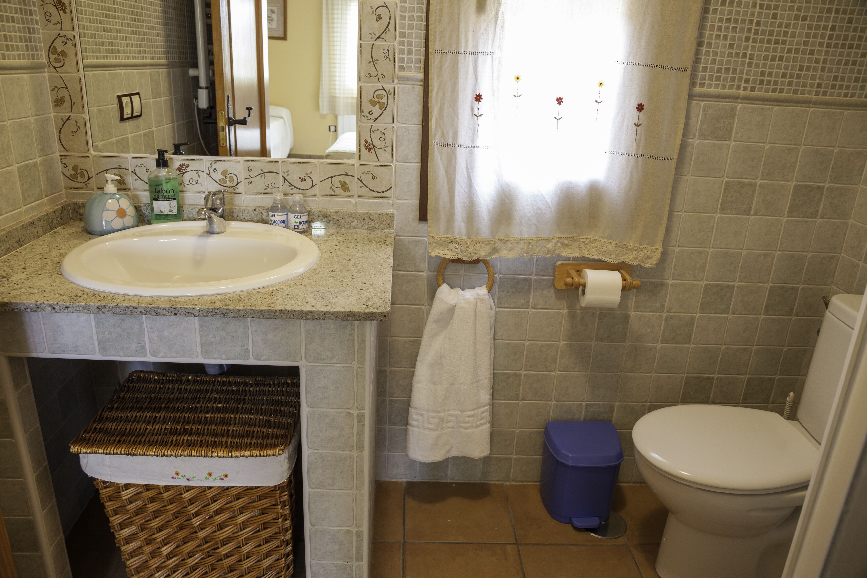 Baño con lavamanos, inodoro y un cubo de basura azul.
