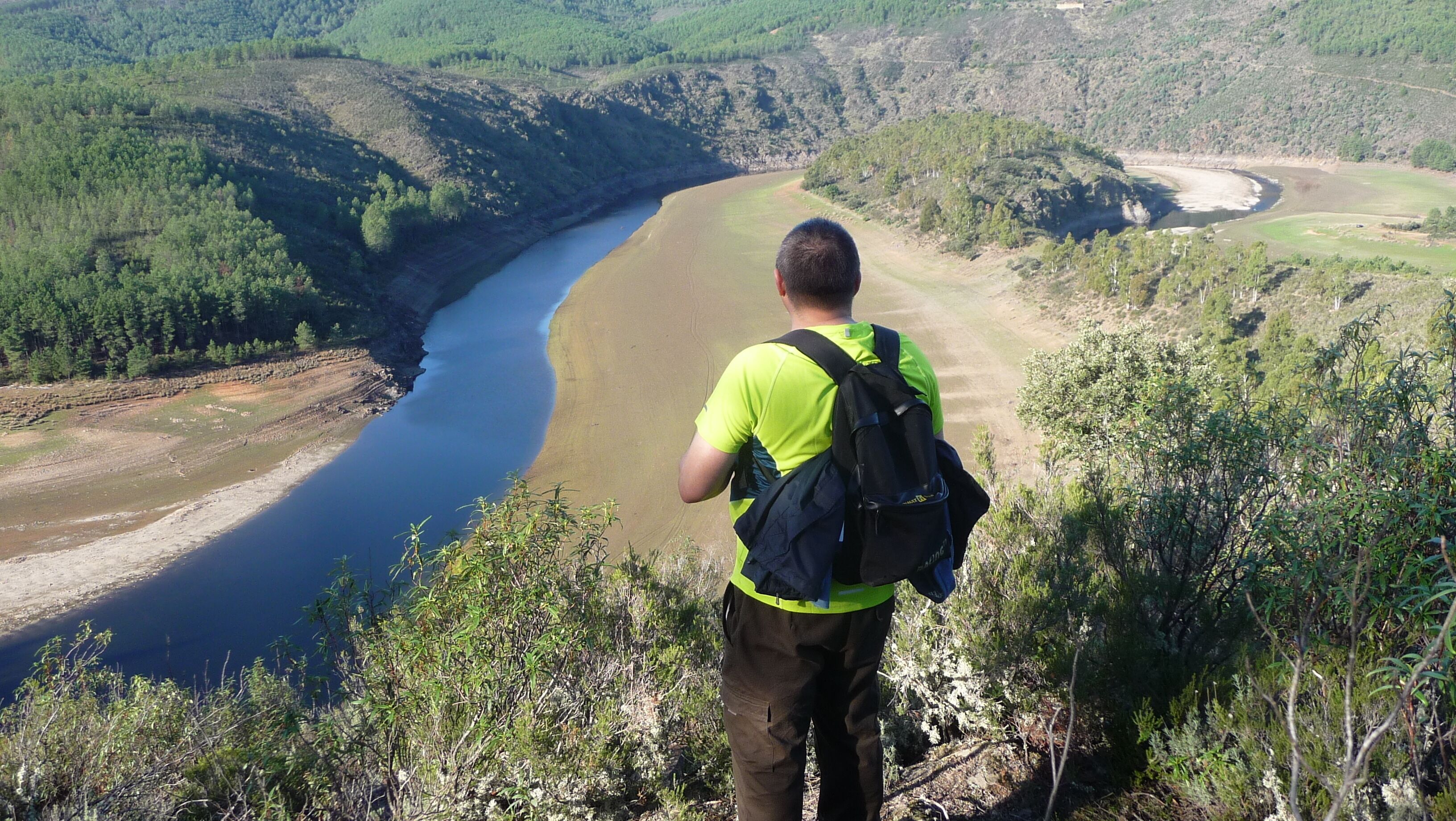 Un excursionista contempla un valle fluvial con denso bosque y colinas.