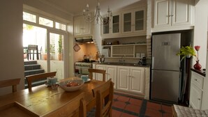 A kitchen with white cabinets, a stainless steel refrigerator, a dining table with chairs, and a chandelier. - A spacious and luxurious three-bedroom house with courtyard and roof deck (Cape Town)