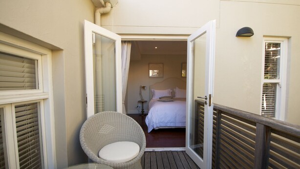 A balcony with a wicker chair, a wooden deck, and a bedroom visible through an open door. - A spacious and luxurious three-bedroom house with courtyard and roof deck (Cape Town)
