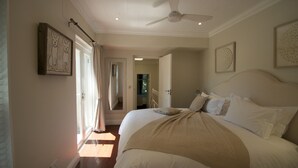 A bedroom with a large bed, a ceiling fan, and a door leading to another room. - A spacious and luxurious three-bedroom house with courtyard and roof deck (Cape Town)