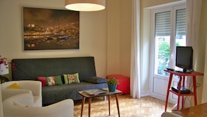 Una sala de estar con sofá, una mesa de centro, un mueble para televisión y una ventana con persianas.