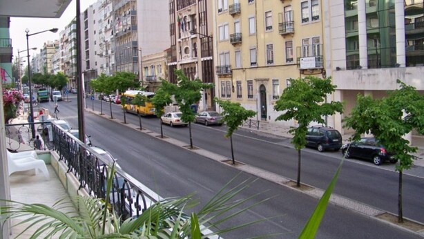 Vista de la calle con edificios de varios pisos, coches aparcados y árboles a lo largo de la vía.