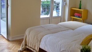 Un dormitorio con cama, ventana, puerta, estante con libros y una planta.