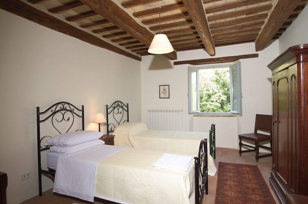 Camera da letto con due letti, soffitto in legno, una finestra con vista su del verde, un termosifone e un armadio.