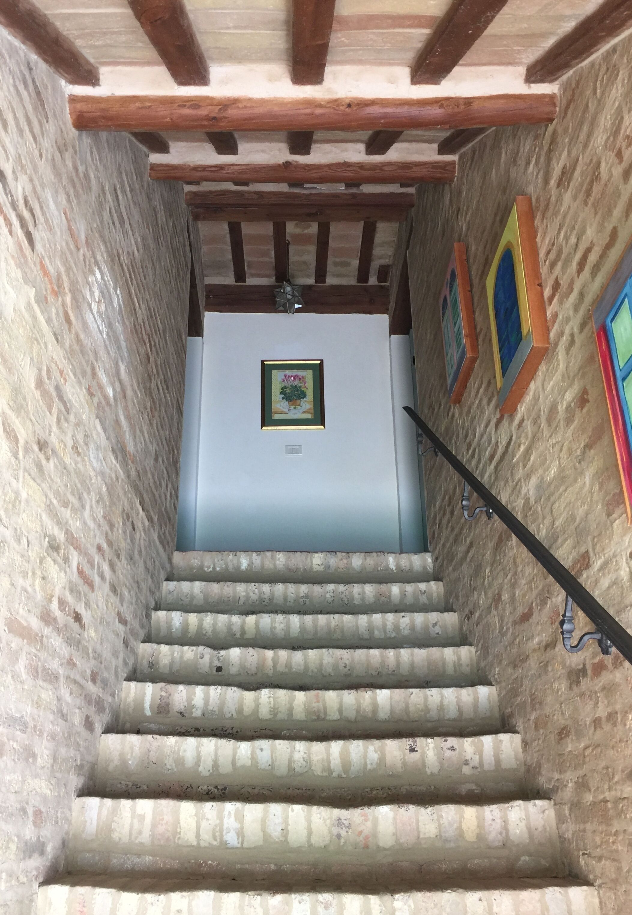 Un escalier avec un plafond en bois et des murs en briques, menant à une pièce où un tableau encadré est accroché au mur.