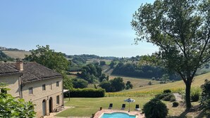 Une piscine avec vue sur des collines ondoyantes et un bâtiment doté d’un toit en tuiles.