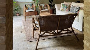 Une pièce chaleureuse avec un haut plafond en bois, un canapé blanc, des fauteuils en osier et des plantes en pot.