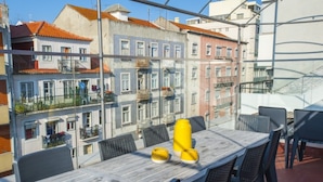 A dining area with a table and chairs, a yellow object on the table, and a view of colorful buildings in the background.