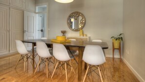 A dining area with a wooden table, four white chairs, a yellow bowl, and a round mirror on the wall.