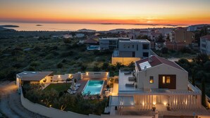 A modern villa with a swimming pool, surrounded by lush greenery and overlooking a coastal landscape during sunset. - Luxury Villa Cinderella with Swimming Pool (Primošten)
