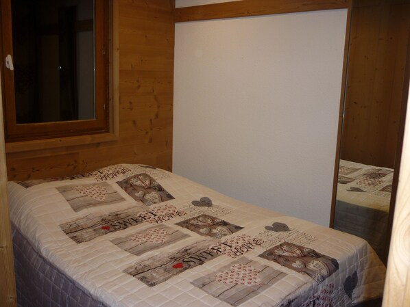 A bedroom with a wooden headboard, a quilted bedspread with floral and heart patterns, and a plain white wall. - At the foot of the slopes, The white queen, 2 separate bedrooms, WIFI (Les Belleville)