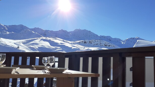 Una mesa con dos copas de vino y un plato, con montañas nevadas y un cielo azul despejado de fondo.