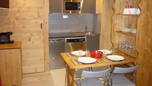 Una cocina compacta con microondas, lavaplatos y lavamanos. Cuenta con una mesa de comedor con sillas, y un juego de platos y vasos.