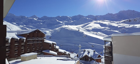 A snow-covered mountain resort with a ski lift, buildings, and a clear blue sky.