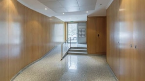 En gang med træpaneler, gelænder i metal og et flisegulv, der fører til en elevator.