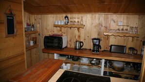 Une cuisine compacte aux murs en bois, équipée d’un four à micro-ondes, d’une machine à café, ainsi que de divers plats et ustensiles de cuisine.