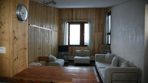 Une pièce aux murs lambrissés, avec une table en bois, deux canapés, un téléviseur et une fenêtre avec des rideaux.