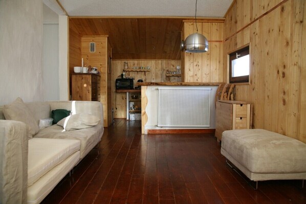A cozy room with a wooden interior, a sofa, a small table, and a kitchen area with a radiator.
