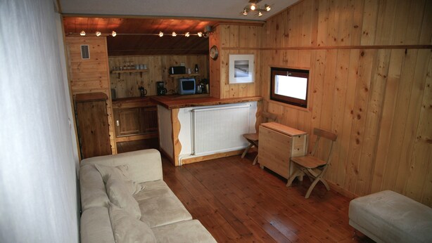 L’intérieur chaleureux d’un chalet, avec un revêtement en bois, un canapé, une petite table et un coin cuisine.
