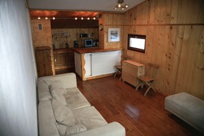 A cozy cabin interior with a wooden interior, a sofa, a small table, and a kitchenette area.