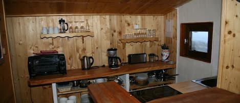 Een keuken met houten lambrisering, een inbouwoven, een koffiezetapparaat en planken met bekers en glazen.