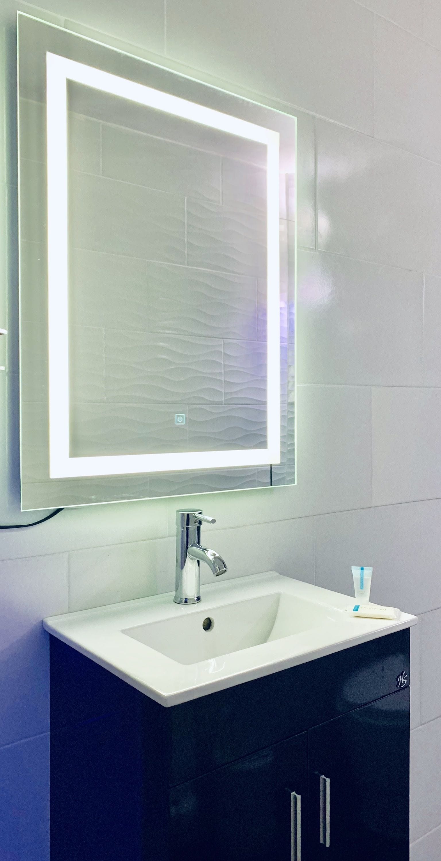 Un baño con un lavamanos blanco, un espejo con luz y un mueble negro.
