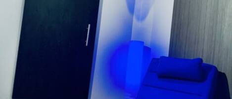 Una habitación con una mesa de masaje azul, una puerta corredera y una lámpara fijada a la pared.