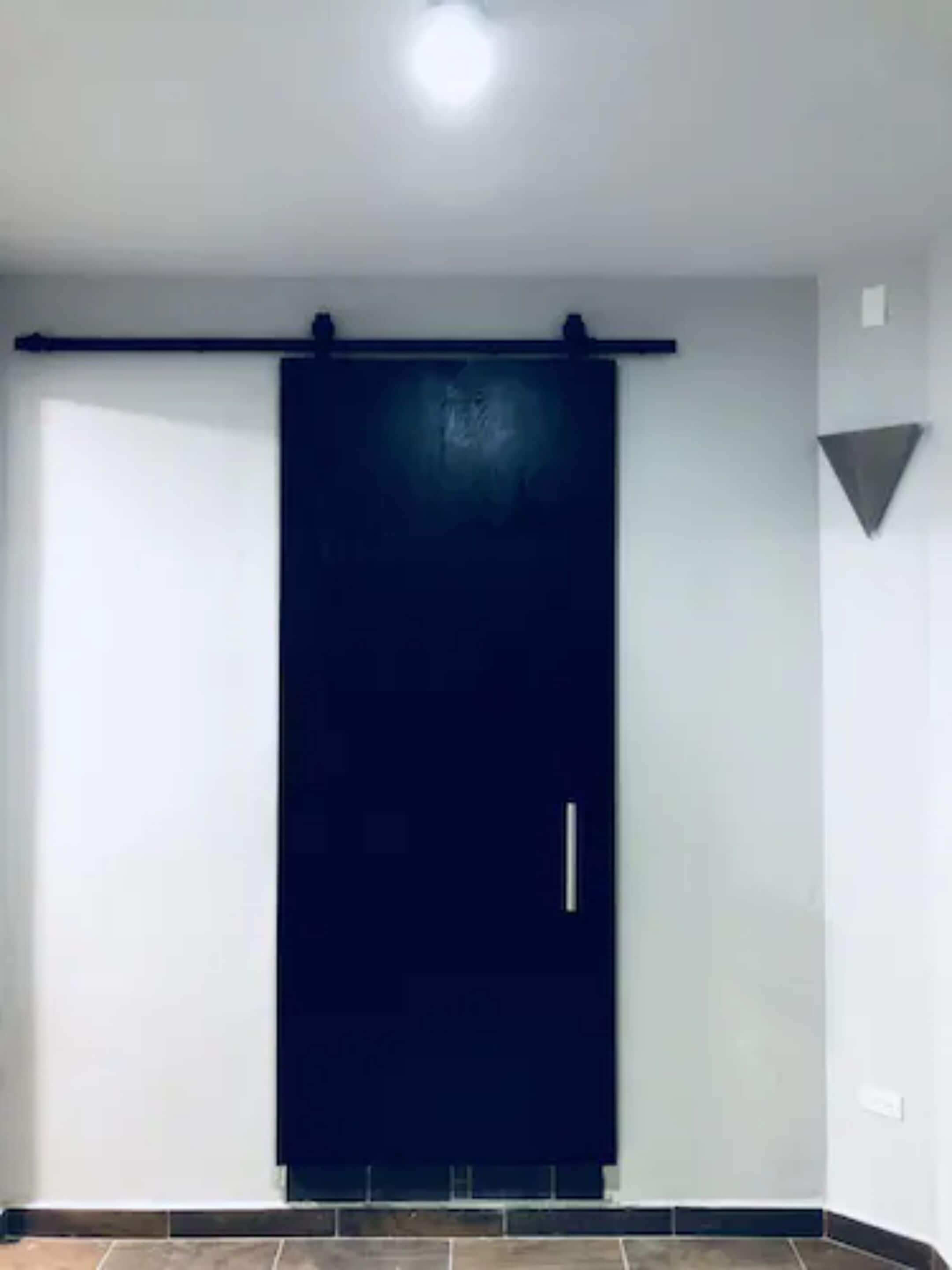 Una habitación con una puerta corredera oscura, paredes blancas y suelo de baldosas.