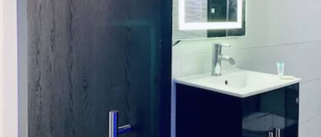 Une salle de bain moderne avec une porte en bois foncé, un lavabo blanc avec un miroir et des meubles noirs.