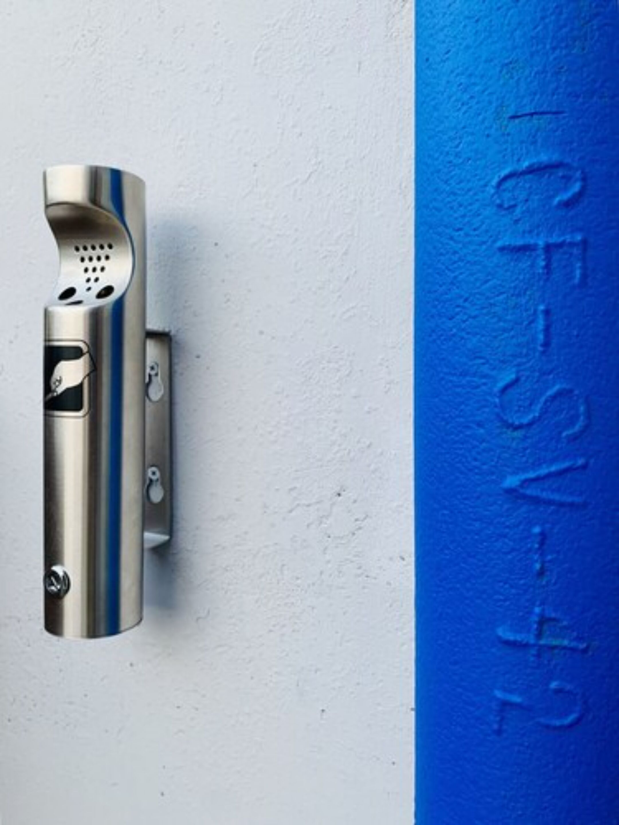 A metallic object with a keyhole and a blue stripe, mounted on a textured wall.