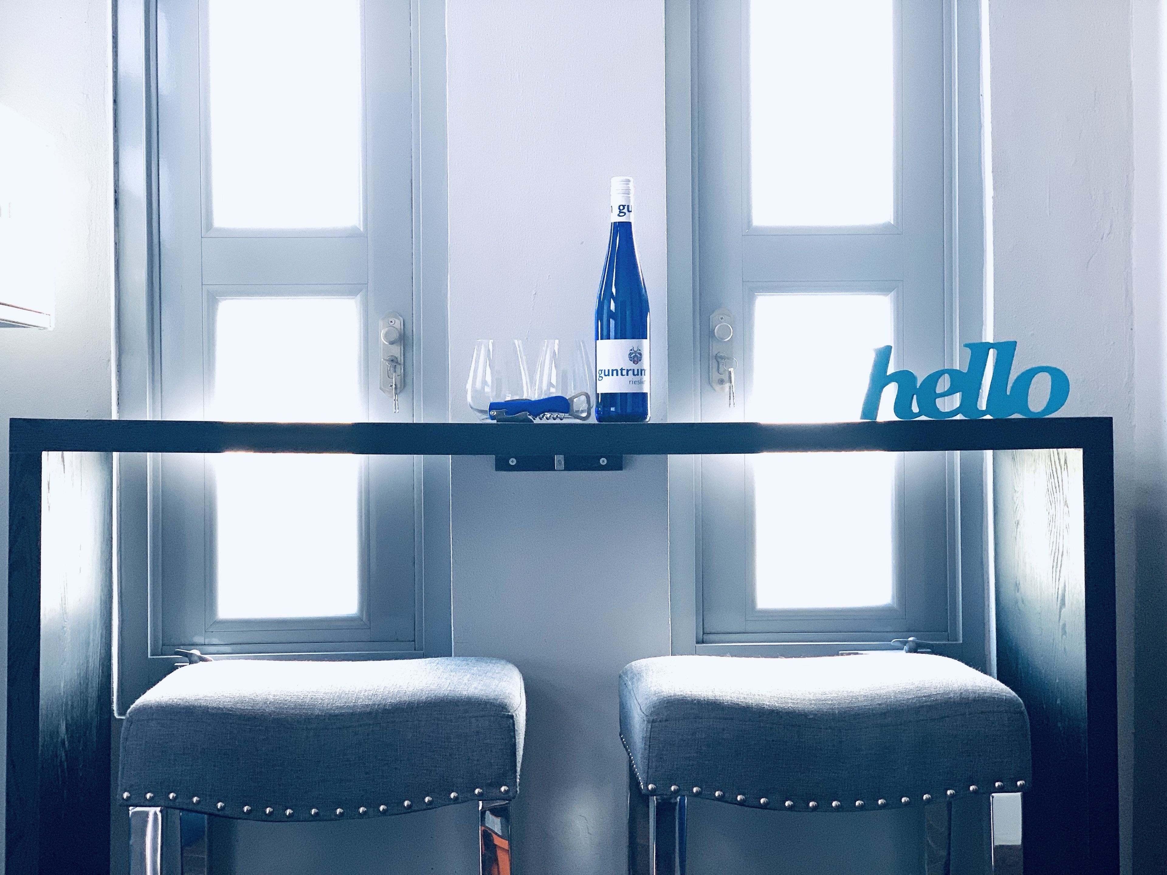 Et værelse med to vinduer, et bord med en flaske og glas, og et skilt med teksten 'hello'.