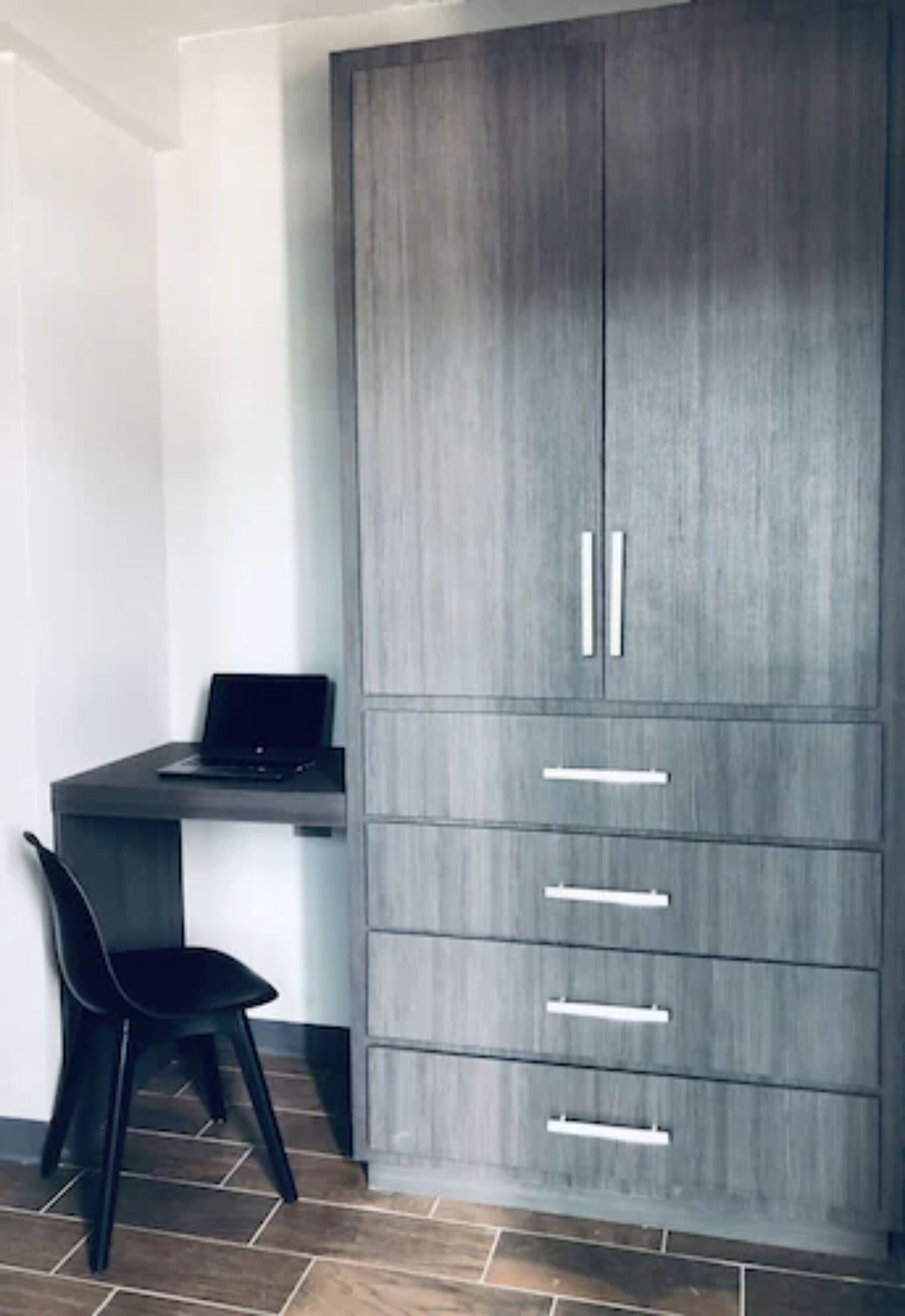 Een moderne kamer met een grijze kast, een zwarte stoel en een laptop op een bureau.