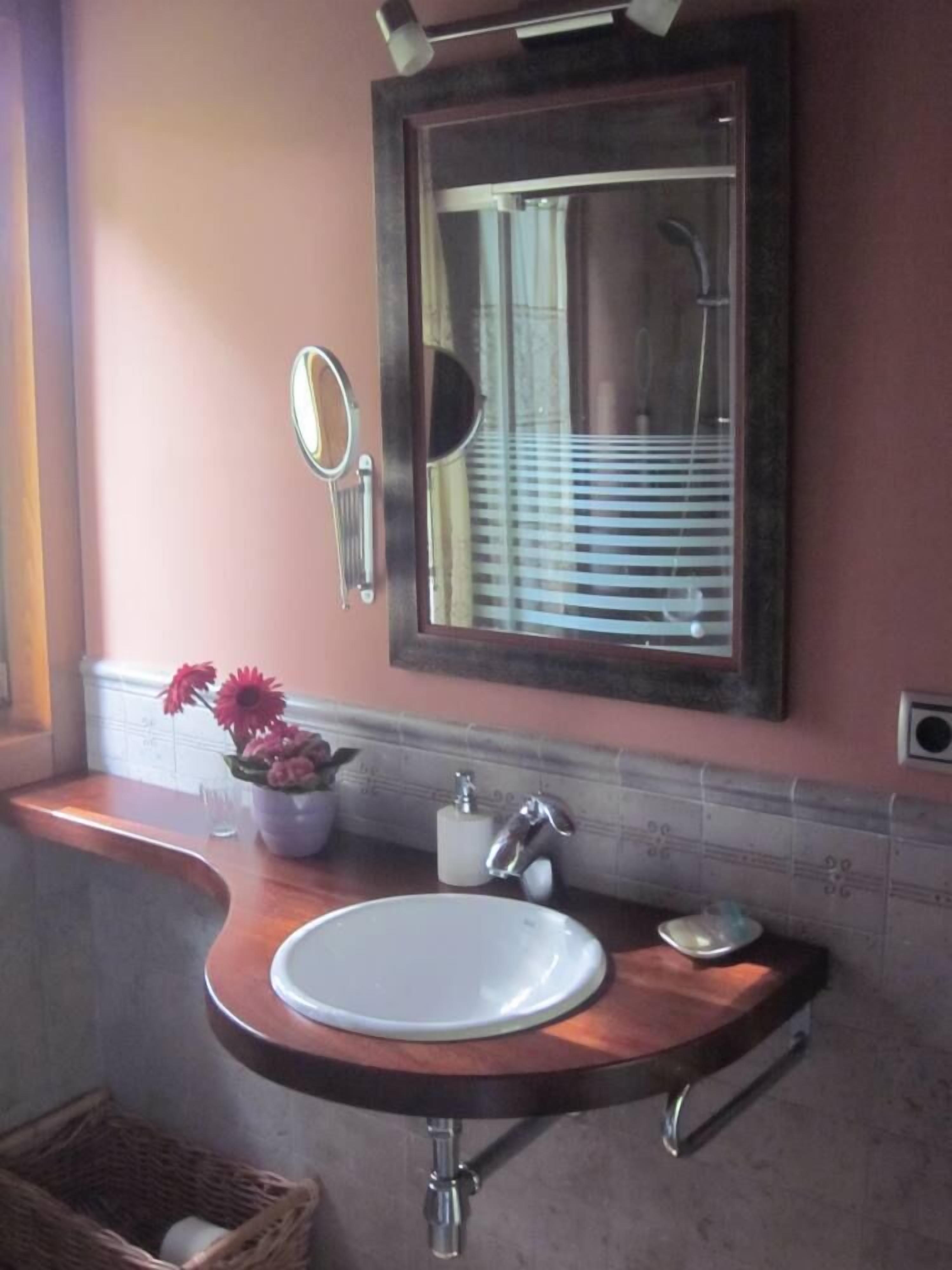 Un baño con lavamanos redondo, un espejo y una ventana con persianas.