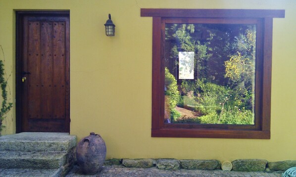 A yellow building with a wooden door and a window with a view of greenery.