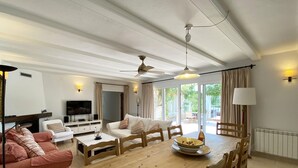 Een ruime woonkamer met een houten eettafel, witte banken en een televisie.