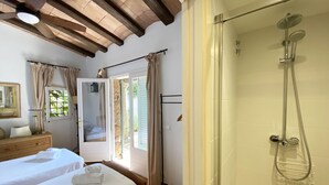 Een slaapkamer met een bed, nachtkastje, spiegel en douche met glazen deur.
