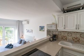 A modern kitchen with white cabinets, a built-in microwave, and a large window overlooking a balcony. - Paraíso Golden Mille- Estepona Studio (Estepona)