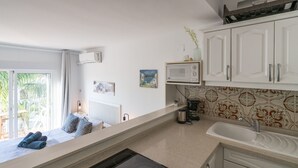 Une cuisine compacte équipée d’une cuisinière intégrée, d’un four à micro-ondes et d’un évier. Une fenêtre offre une vue sur la verdure environnante.