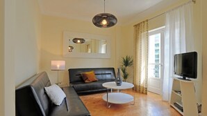 Un salon avec un canapé noir, une petite table basse blanche, un téléviseur posé sur un meuble et un grand miroir accroché au mur.