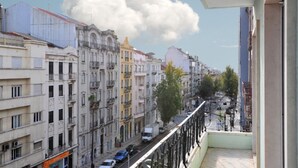 Un balcon donnant sur une rue de la ville, des immeubles et un ciel dégagé.