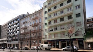 Un immeuble à plusieurs étages doté de balcons, d’une devanture de magasin et de voitures garées.