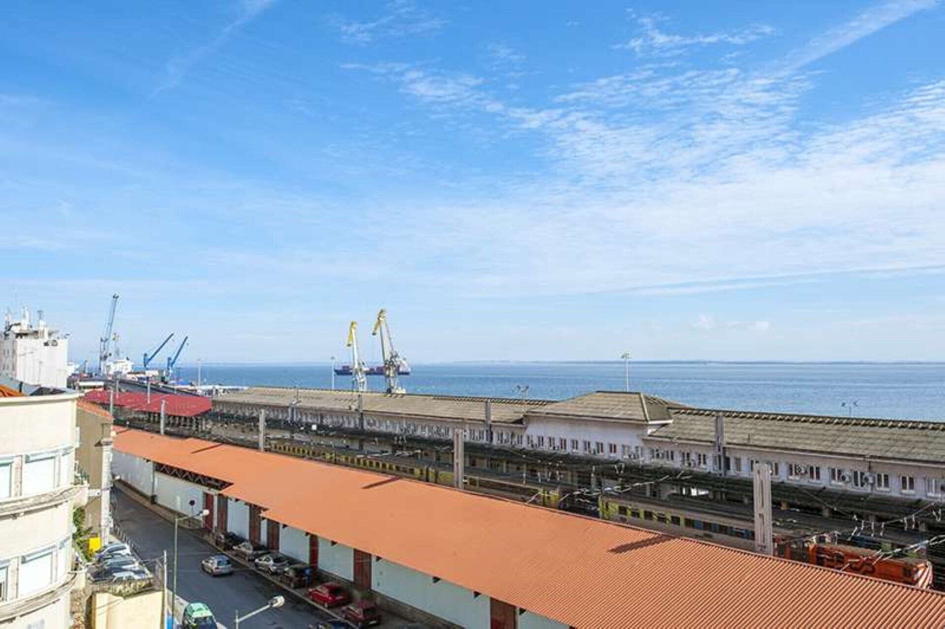 A coastal industrial area with shipping cranes, a port, and a building with a red roof.