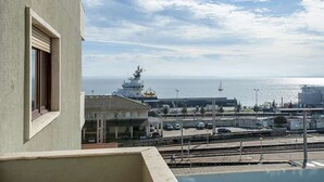 Vista des d'un balcó sobre un port amb un vaixell, una estació de tren i una riba llunyana.