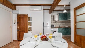 Zona pranzo con tavolo rotondo imbandito per quattro persone, cucina con elettrodomestici moderni e travi in legno al soffitto.