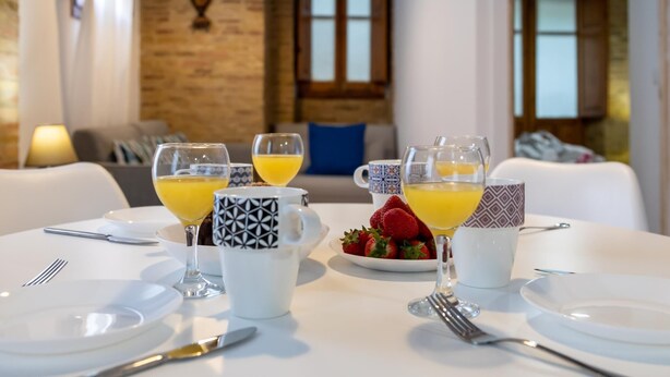 Impostazione da colazione con un tavolo apparecchiato per due, con una ciotola di fragole, due bicchieri di succo d'arancia e un teiera.