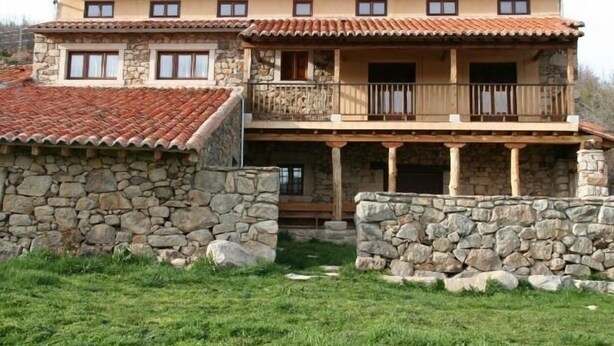 A two-story stone house with a balcony, stone walls, and a tiled roof.